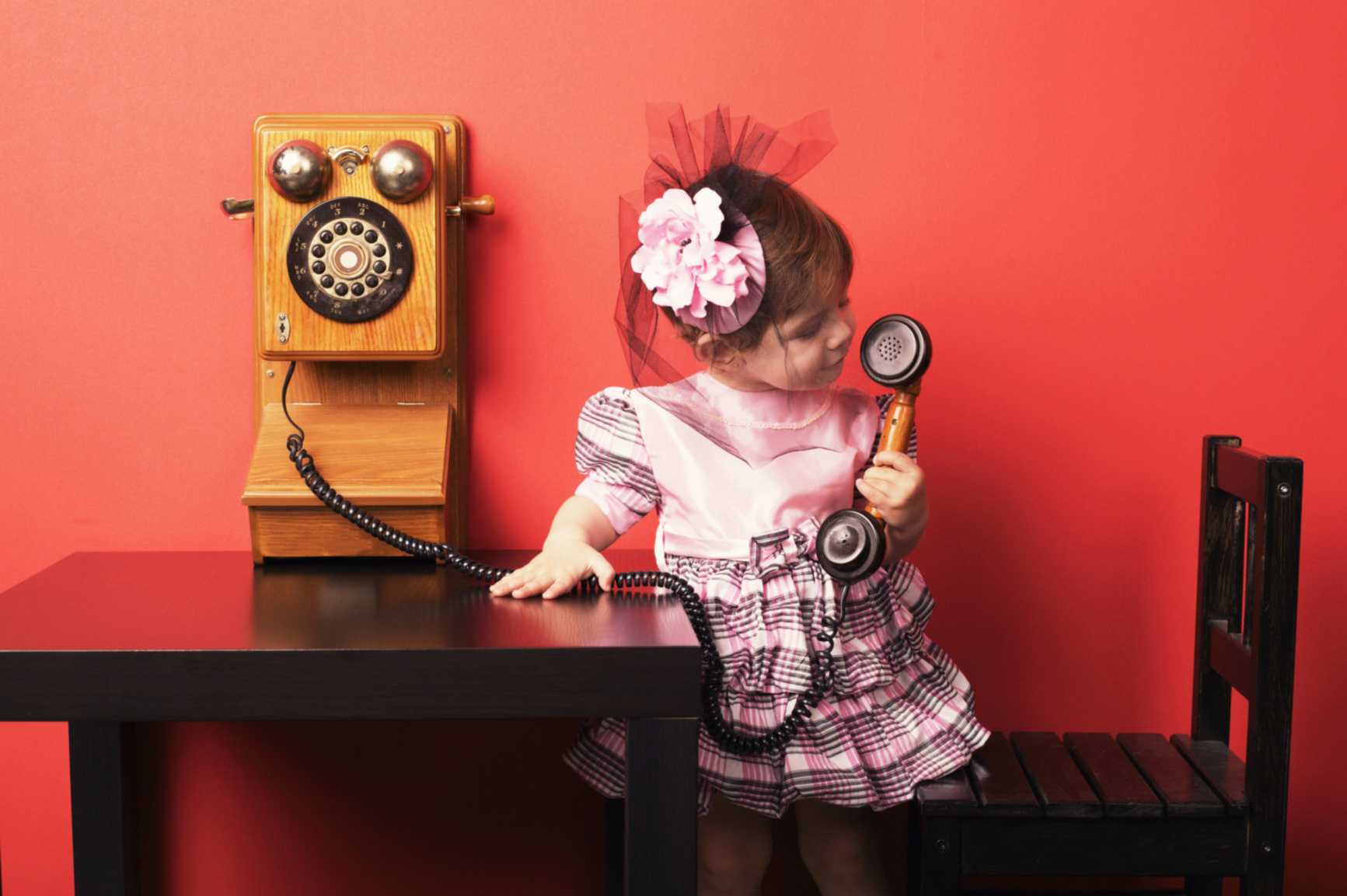 Little girl standing on chair, holding and looking at receiver of an old-fashioned wall phone.